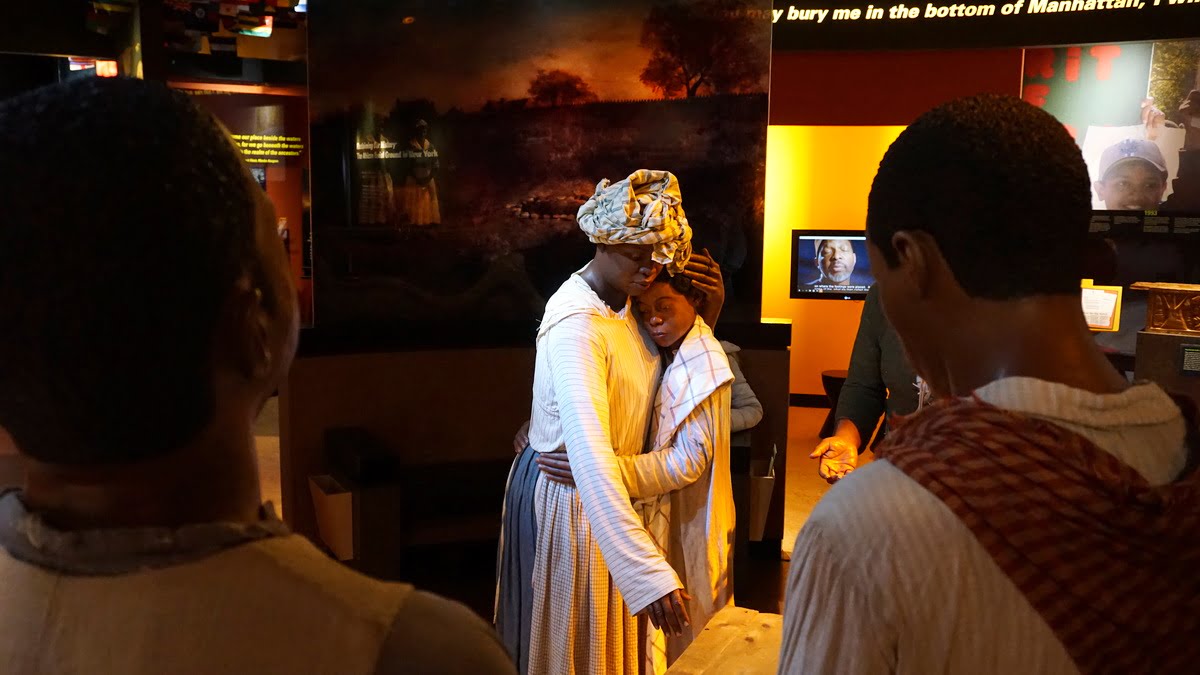 Picture of the African Burial Ground National Monument Wax figures, with a mom and child in the center and further from the camera, with two adult men with heads to the back of the camera and closer to the camera. National Parks in New York City - New York Weekend Trip Travel Guide