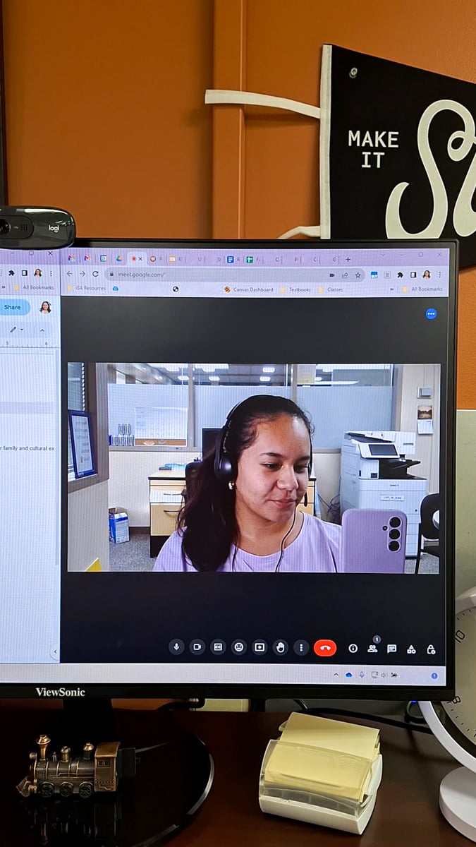 Picture of Yasmin in front of her computer with her headset and webcam.