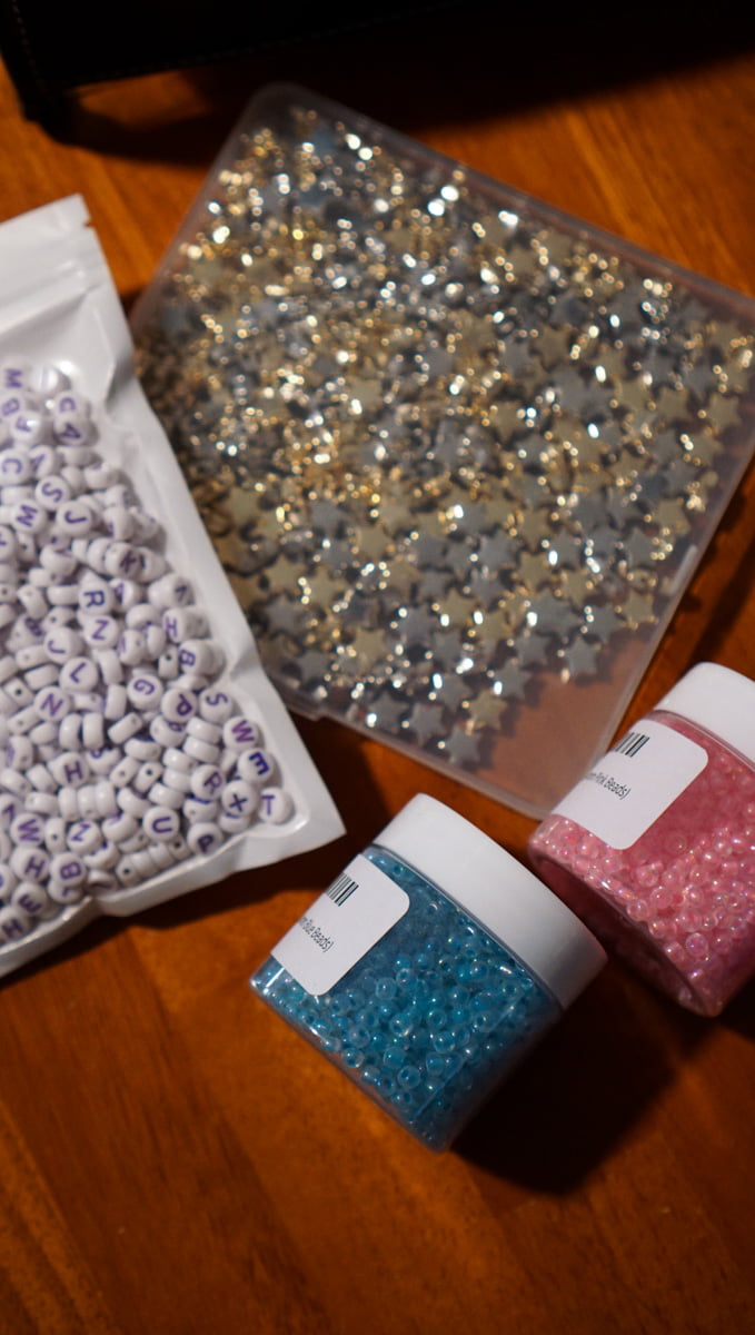 Decorative and letter beads that will be used to make friendship bracelets for Taylor Swift's Eras concert. Beads are star shaped, and there's also pink and blue beads that glow in the dark from Amazon.