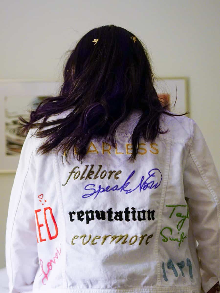 Yasmin is facing away from the camera and is showing off her white jacket with embroidered Taylor Swift album titles | Outfit Inspiration for Taylor Swift: The Eras Tour 